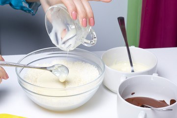 Woman adds condensed milk to coconut chips. Ingredients for dessert are on the table. Cooking sweets with coconut and condensed milk. In a glaze of white and black chocolate.