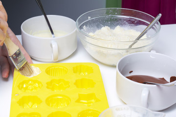 A woman lubricates a silicone mold with melted white chocolate. Ingredients for dessert are on the table. Cooking sweets with coconut and condensed milk. In a glaze of white and black chocolate.