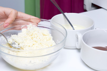 A woman mixes condensed milk and coconut chips. Ingredients for dessert are on the table. Cooking sweets with coconut and condensed milk. In a glaze of white and black chocolate.