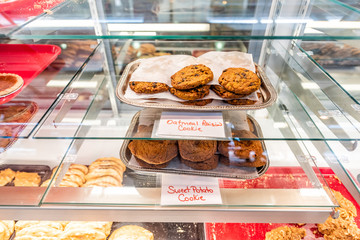 Many different cookies with signs on trays display in street food market or bakery cafe with oatmeal and sweet potato biscuits on glass window