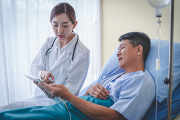 Asian female doctor with male patient is checking the results from the tablet.