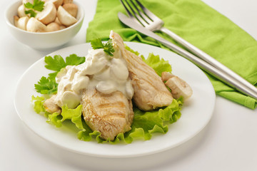 Fried chicken breast with cream sauce and mushrooms on a white plate and a green napkin. White background