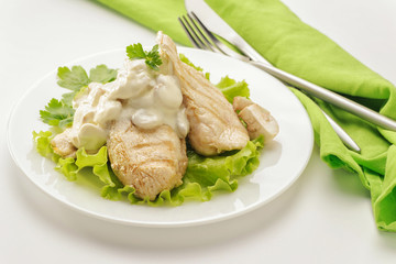 Fried chicken breast with cream sauce and mushrooms on a white plate and a green napkin. White background