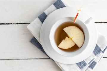 Apple juice or apple tea in white cup on wooden background.