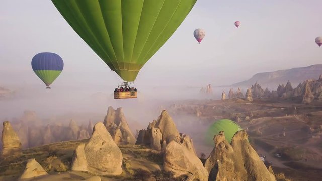 hd aerial drone dolly top down, zooming in hot air balloon and people in the basket, over chi&radic;&part;ney rocks on a hill, in Cappadocia, Nevsehir, Turkey