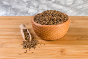 Caraway seeds in wooden scoop and bowl on bamboo desk. Top view.