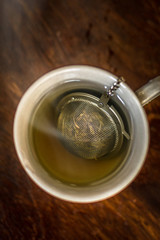 Cup of Tea with infuser in hot smoky water with green tea, mint herbs and honey on a dark wooden background