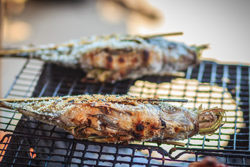 Salt coated tilapia fish that grilled on charcoal stove. Roasted tilapia fish with salt in bamboo stick for sale on the street in the market.