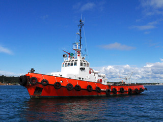 Fototapeta premium Red Tug at anchor in estuary bay awaiting next towing operation.