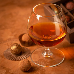 A glass of brandy and chocolate candy dark background. Alcoholic drink and elite chocolate food concept. Square frame