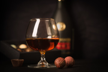 A glass of brandy and chocolate candy on a dark background. Alcoholic drink and elite chocolate food concept.