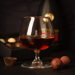 A glass of brandy and chocolate candy on dark background. Alcoholic drink and elite chocolate food concept. Square frame