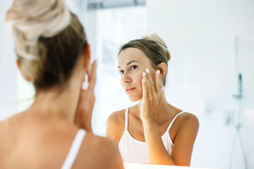 Woman applying face cream in bathroom