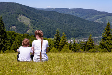 Mother and young son sitting on grass on the background of coniferous forest and mountains