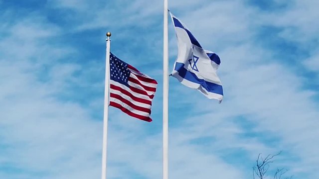 American and Israeli flags waving in the wind with a blue sky with puffy white cloud background