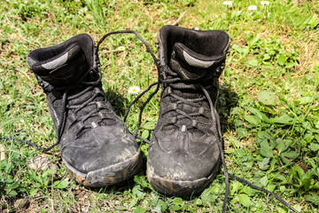 Old hiking boots with untied laces stand on green grass