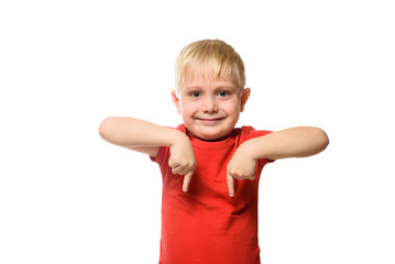 Smiling little blond boy in a red shirt stands and shows index fingers down. Isolate on white background.