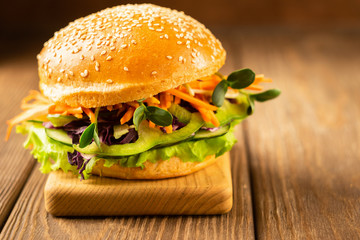 Appetizing veggie burger with fresh raw vegetables close-up on a dark wooden background. Healthy eating concept.