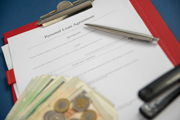 Personal loan agreement  paper form with pen, money and stapler. Defocused business background.