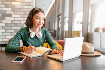 Young happy business asian woman taking notes in notebook and working with laptop pc or computer....