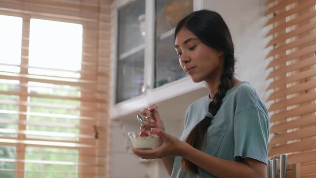 Portrait of young asian woman eating yogurt in kitchen at home.