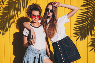 Candid shot of two lovely hipster women in glasses and denim clothes standing under the shadow of...