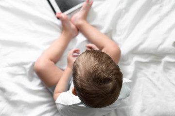 boy on a bed with white linens playing in the tablet