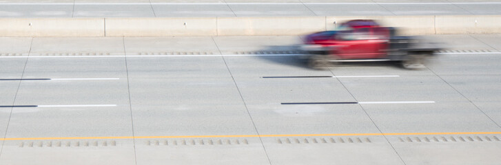 A blurred motion photo of a red flatbed truck on a highway.