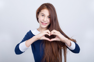 Beautiful girl shows hands the sign of the heart, standing on a light background.