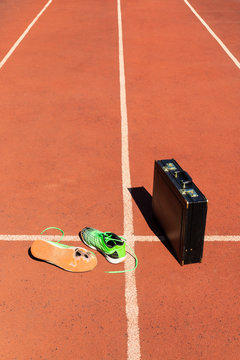A black briefcase and a pair of broken green running shoes on a running track symbolizing competition, challenge and burnout in work and business