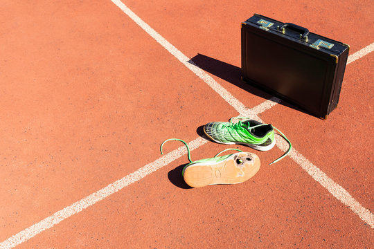 A black briefcase and a pair of broken green running shoes on a running track symbolizing competition, challenge and burnout in work and business