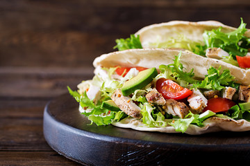 Pita bread sandwiches with grilled chicken meat, avocado, tomato, cucumber and lettuce served on  wooden background. Close up. Healthy fast food concept.