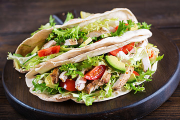 Pita bread sandwiches with grilled chicken meat, avocado, tomato, cucumber and lettuce served on  wooden background. Close up. Healthy fast food concept.
