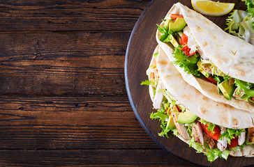 Pita bread sandwiches with grilled chicken meat, avocado, tomato, cucumber and lettuce served on  wooden background. Close up. Top view. Healthy fast food concept.
