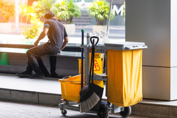 Janitorial mop bucket with caution wet floor sign and worker in back.