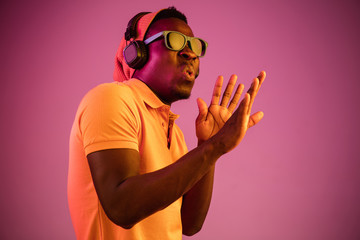 The young handsome serious sad hipster man listening music with headphones at studio with neon lights. Disco, night club, hip hop style, positive emotions, face expression, dancing concept
