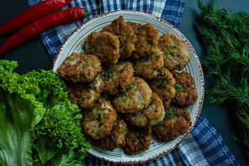 Pork cutlets on a plate with greens and vegetables on a black background. View from above.