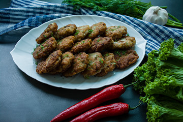 Pork cutlets on a plate with greens and vegetables on a black background. View from above.