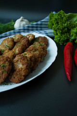 Pork cutlets on a plate with greens and vegetables on a black background. View from above.