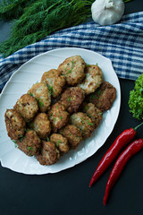 Pork cutlets on a plate with greens and vegetables on a black background. View from above.