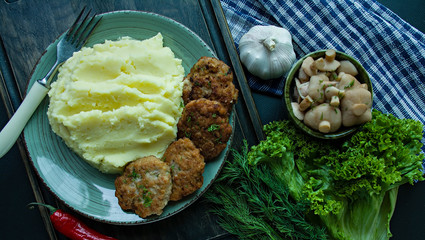 Pork cutlets with mashed potatoes, greens and fresh vegetables on a black background. View from above.