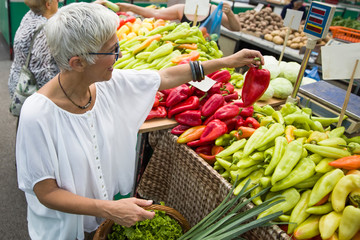 Good-looking senior woman wearing glasses buys pepper on market