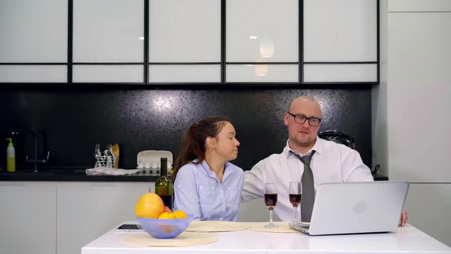 An adult couple have dinner at home in the kitchen. Fun after work business family. drink red wine