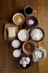 Different ingredients for baking - milk, butter, eggs and flour, cottage cheese, sour cream, brown sugar, cocoa, butter on rustic background, top view