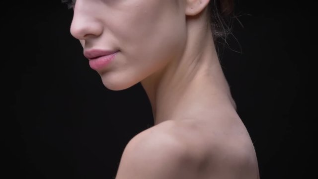 Portrait in profile of young and slim caucasian girl with nude make-up watching in camera over her shoulder on black background.