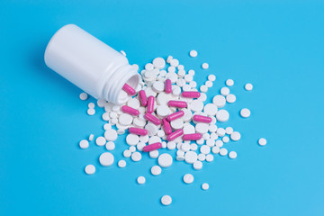White and pink pills, tablets and white bottle on blue background.