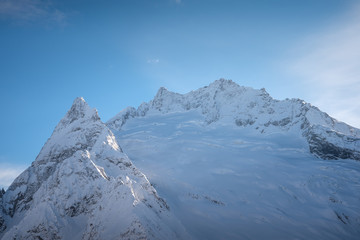 Fototapeta na wymiar mountain peaks of Dombai mountains covered with snow surrounded by thick clouds against the blue sky. February 2019