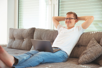 Handsome man works at home with his laptop on couch