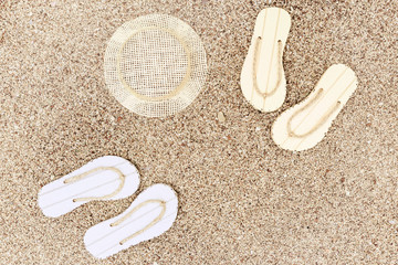 Sun hat and pair of flip-flops on sandy beach under bright sun. Copy space.