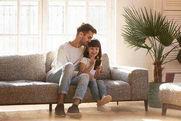 Happy dad embracing kid daughter enjoy using smartphone at home